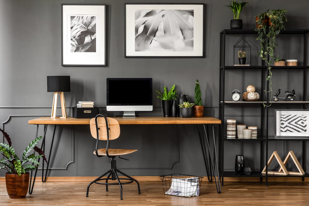 Posters in natural home office Posters on grey wall above wooden desk in natural home office interior with plants and lamp